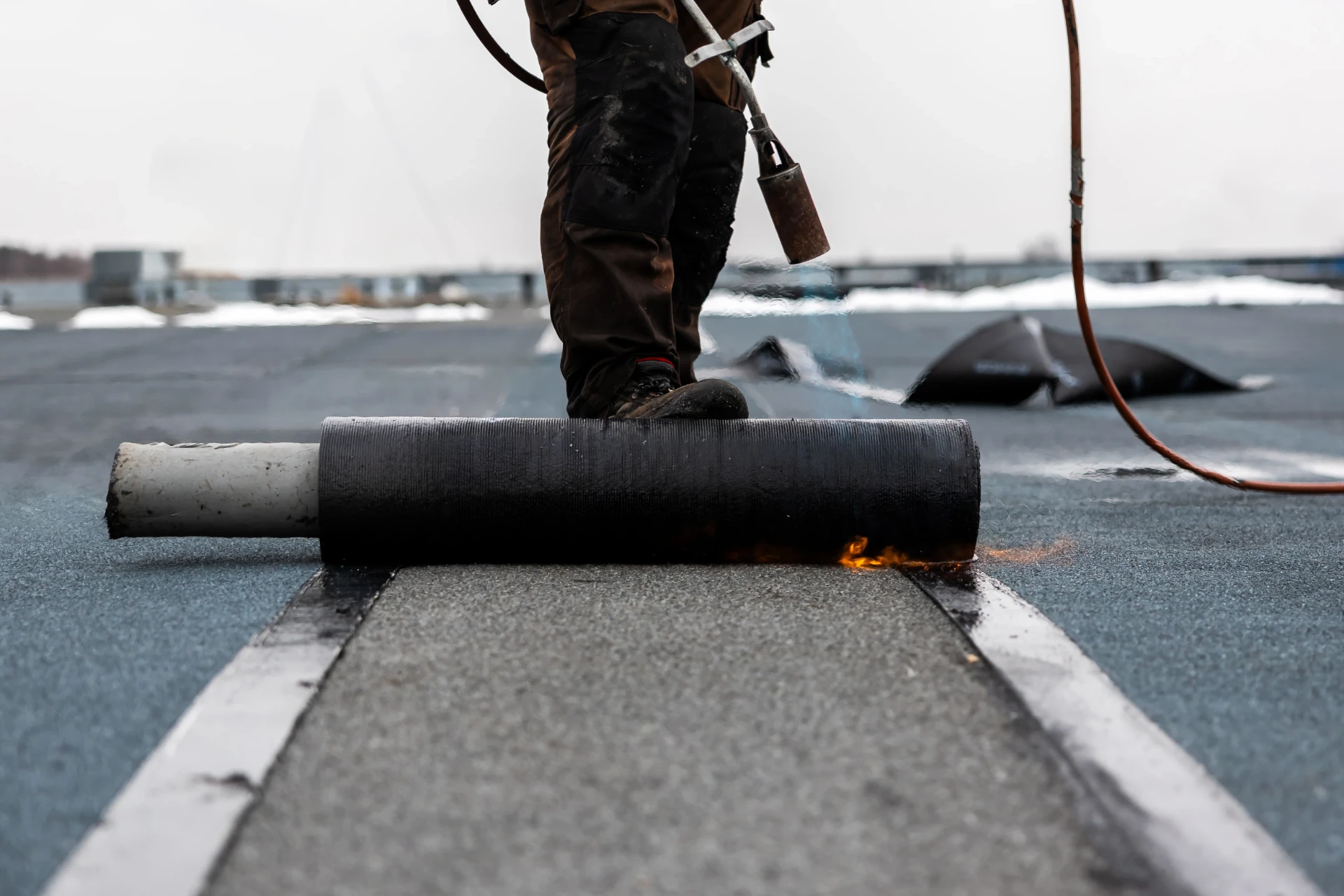 Roofer bonding torch-on felt across a flat roof during a full re-cover