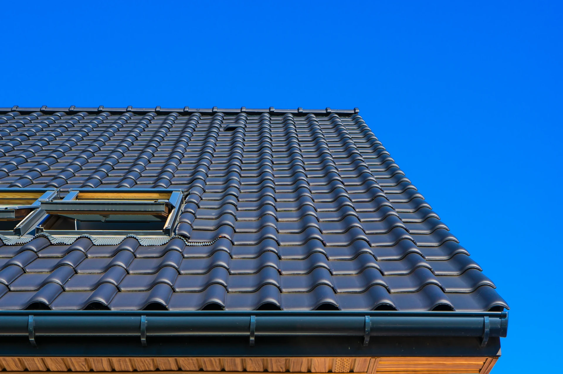 Dark interlocking tiles covering a pitched roof with a roof window and neat guttering