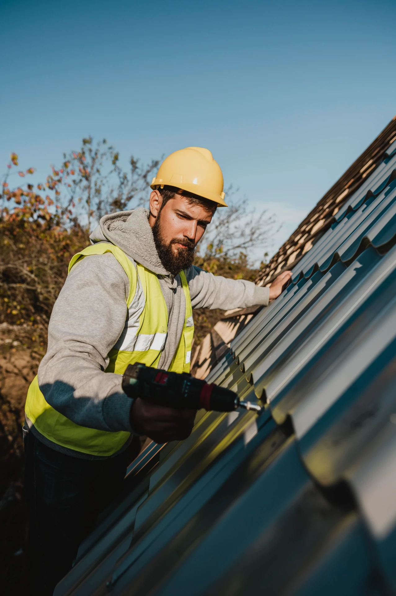 Roofer securing a lead flashing detail at roof level with a cordless drill